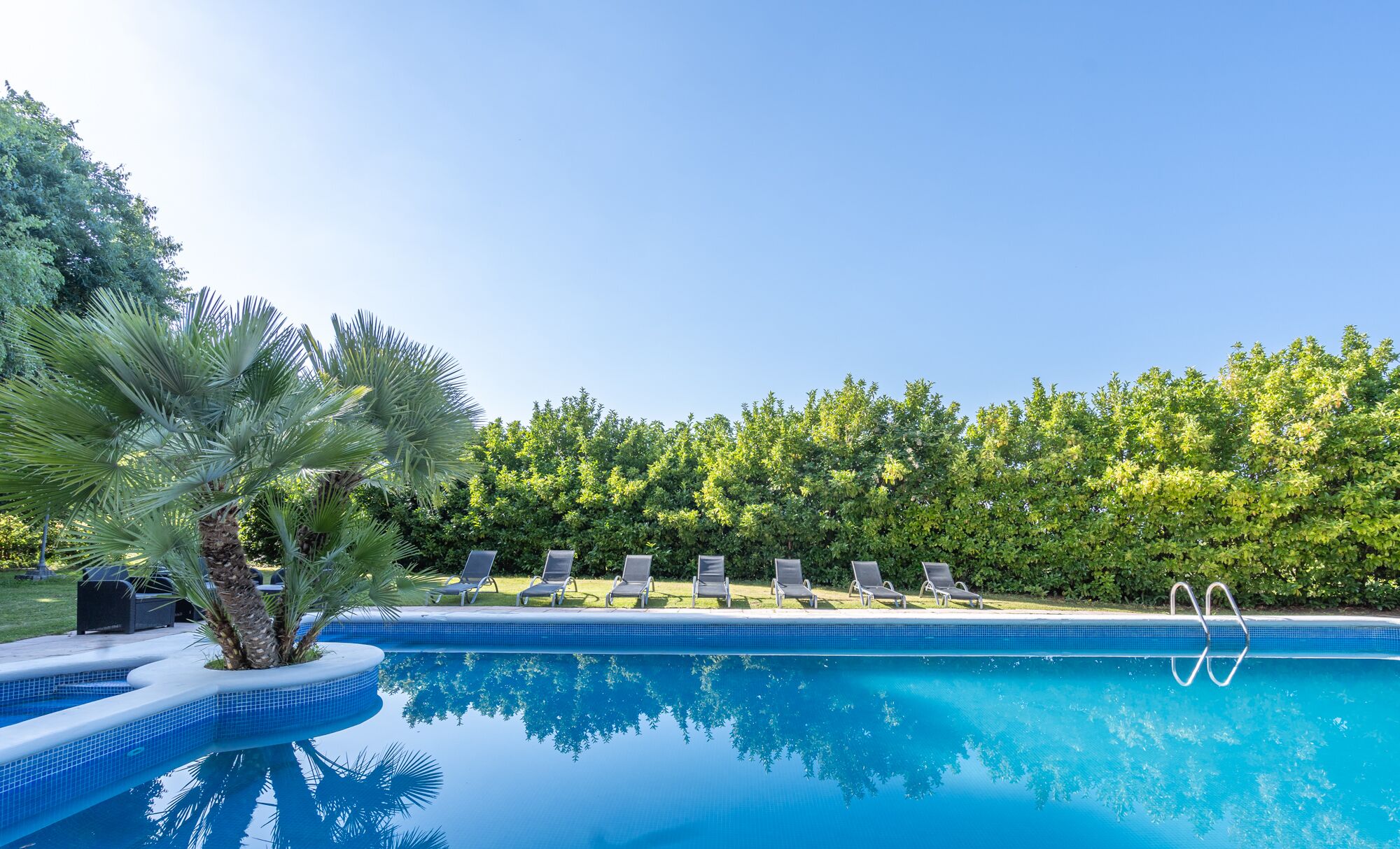 Een buitenzwembad, ligstoelen bij het zwembad