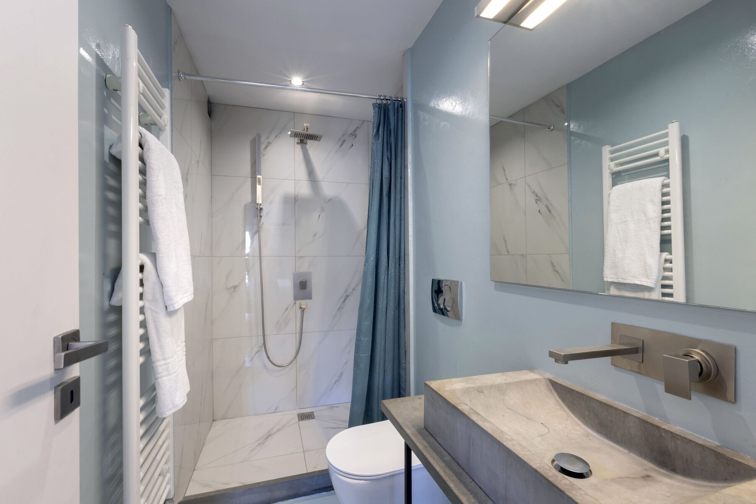 A modern bathroom with a glass shower enclosure, a marble-tiled shower area, a white toilet, and a beige sink with a mirror above it.