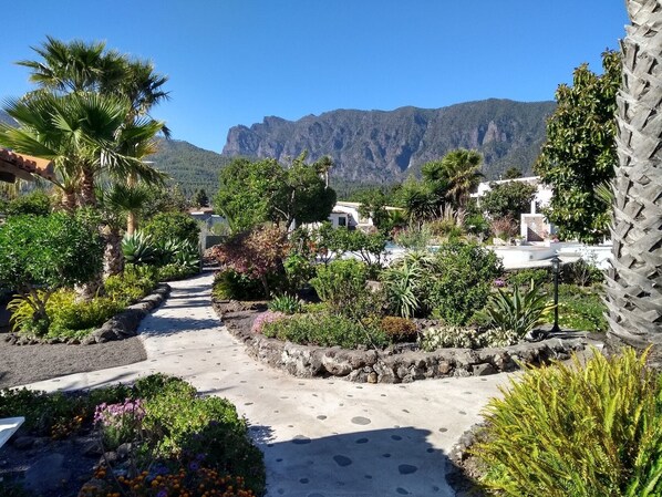 Un sentier de jardin qui mène à un bâtiment blanc, avec une montagne en toile de fond.
