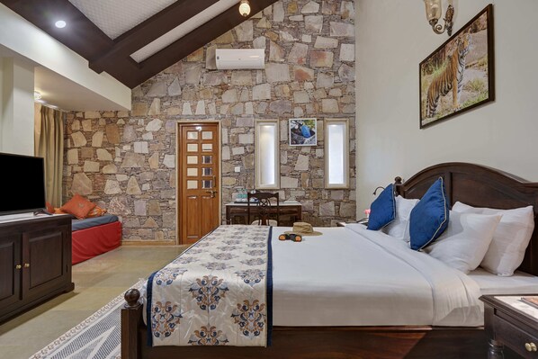 A bedroom with a stone wall, a wooden door, a bed with white bedding, and a television on a cabinet.