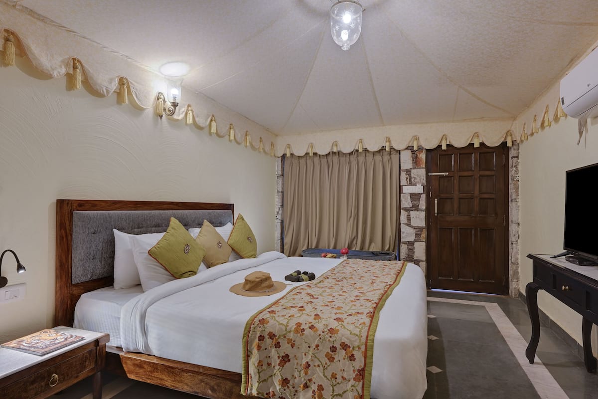 A neatly made bed with a floral bedspread, a wooden headboard, and a pair of slippers on the nightstand.