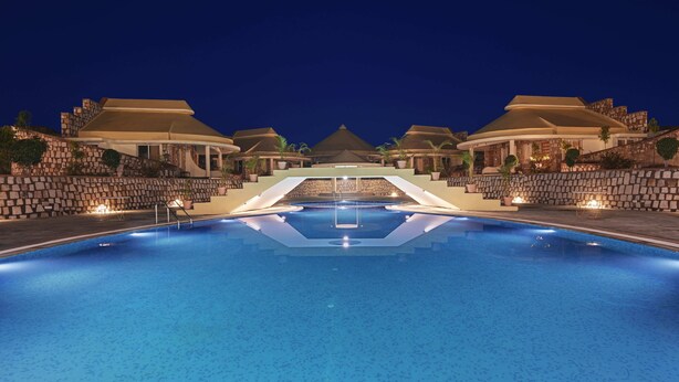 A swimming pool with a central diving platform, surrounded by stone walls and potted plants, under a night sky. - The Sawai Bagh (Sawai Madhopur)