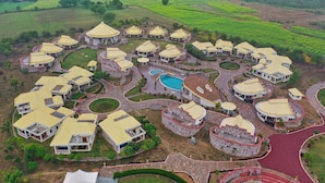 An aerial view of a resort with multiple round-roofed buildings, a central swimming pool, and surrounding green fields. - The Sawai Bagh (Sawai Madhopur)