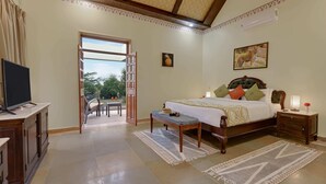 A bedroom with a bed, bedside table, TV, and a view of the outdoors. - The Sawai Bagh (Sawai Madhopur)