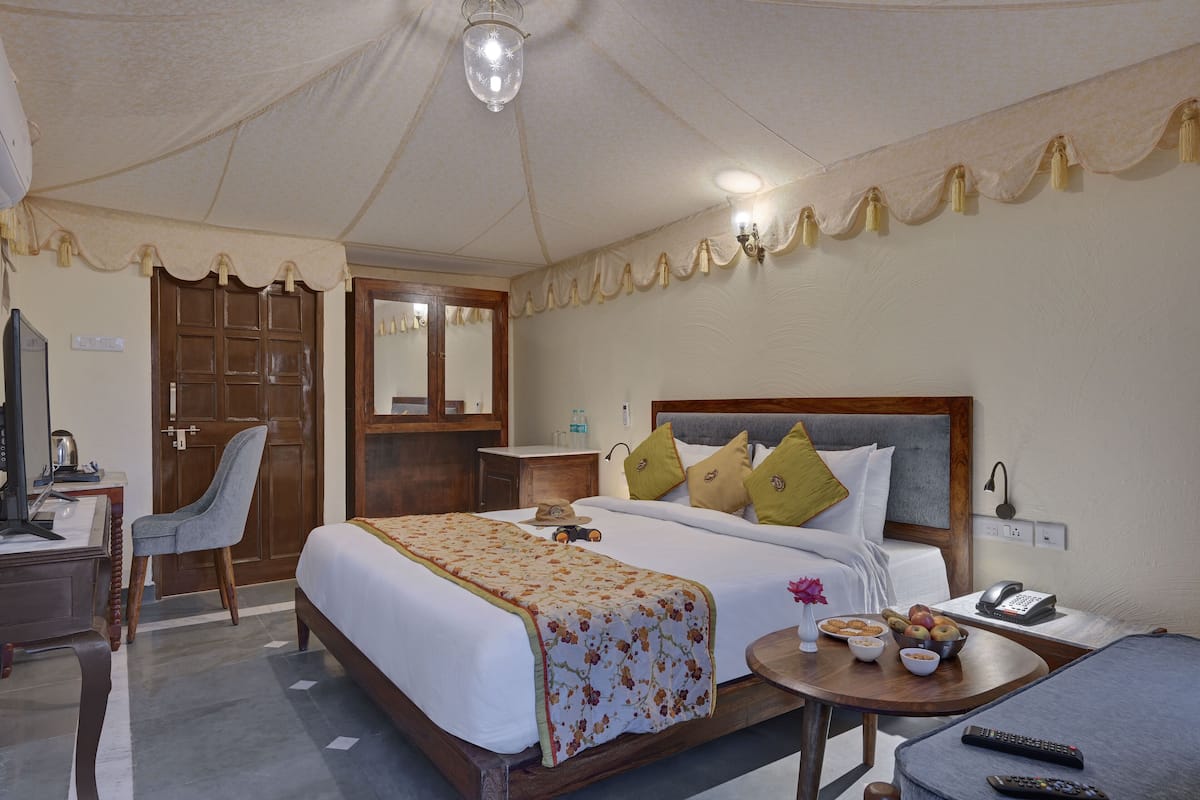 A hotel room with a large bed, bedside table, chair, desk, and a television.