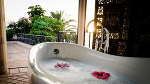 A large bathtub filled with bubbles, two pink flowers, and a balcony with a railing and greenery in the background. - El Refugio Apartments & Villa; El Teide - Honeymoon (La Matanza de Acentejo)