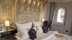A hotel room with an ornate headboard, a bed with white linens, two dark robes, and a window with curtains. - El Refugio Apartments & Villa; El Teide - Honeymoon (La Matanza de Acentejo)