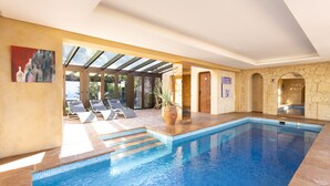 An indoor swimming pool with clear blue water, lounge chairs, and a stone wall. - El Refugio Apartments & Villa; El Teide - Honeymoon (La Matanza de Acentejo)