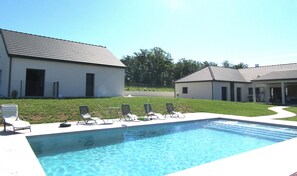 Une piscine avec des chaises longues et un bâtiment doté d’un toit en tuiles.