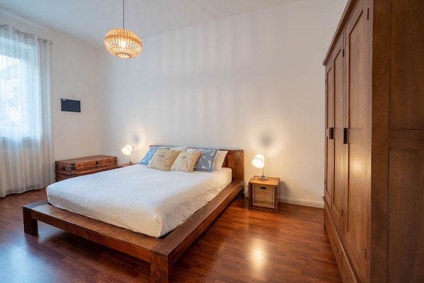 Ein Schlafzimmer mit einem hölzernen Bett, zwei Nachttischen mit Lampen, einem Holzschrank und einer Pendelleuchte.