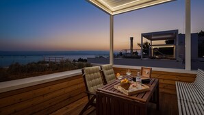 Una terraza de madera con una mesa preparada para dos, con vistas a un paisaje costero.