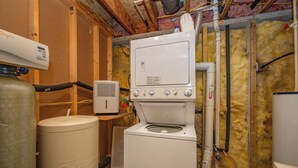 Une buanderie équipée d’un lave-linge et d’un sèche-linge superposés, d’un chauffe-eau et d’un isolant sur les murs.