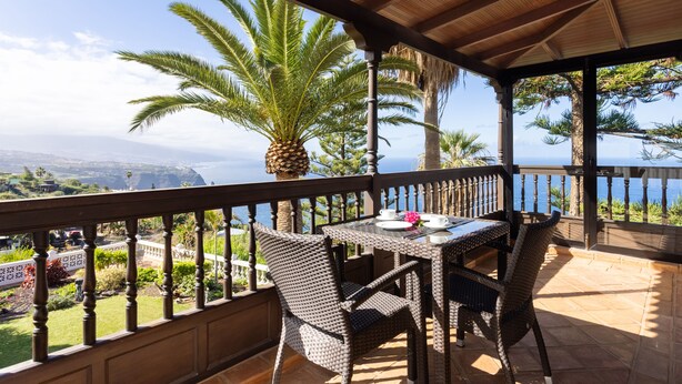 Un espace extérieur abrité, doté d’une table et de chaises, offrant une vue panoramique sur l’océan et les palmiers.