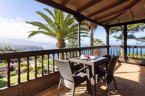 Un espace extérieur abrité, doté d’une table et de chaises, offrant une vue panoramique sur l’océan et les palmiers.