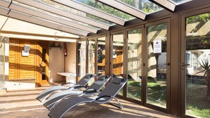 Une véranda avec des portes vitrées, un sauna en bois et des chaises longues.