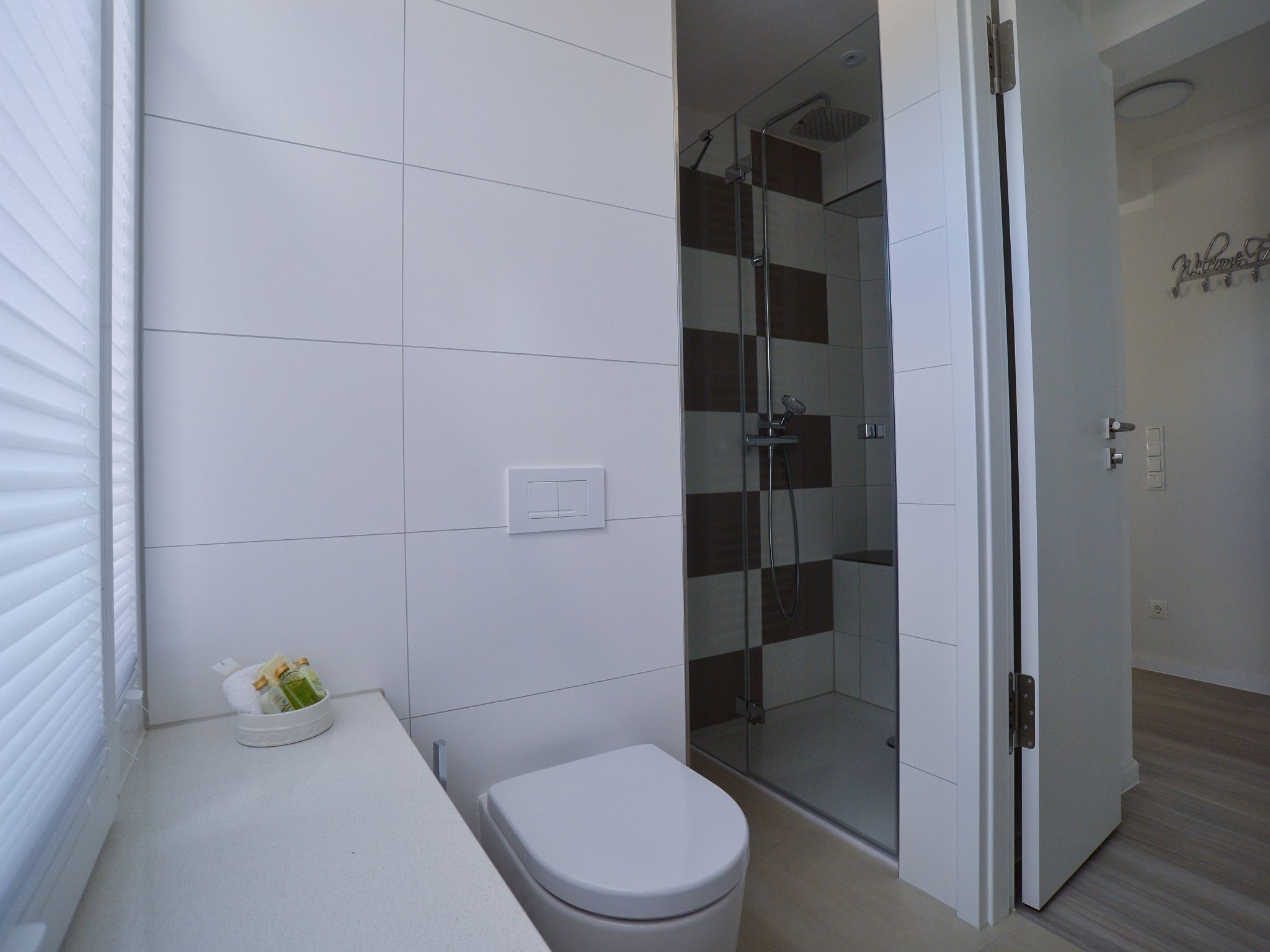 Un bagno moderno con piastrelle bianche, box doccia in vetro, un water e un lavandino con articoli da toilette.