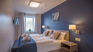A hotel room with a large bed, a bench, a bedside table, and a window with curtains. - Apartment with sea view, 2 bedrooms and balcony (Ostseebad Binz)