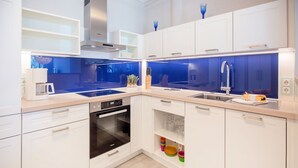 A modern kitchen with white cabinets, a built-in oven, a stainless steel range hood, and a double sink. - Apartment with sea view, 2 bedrooms and balcony (Ostseebad Binz)