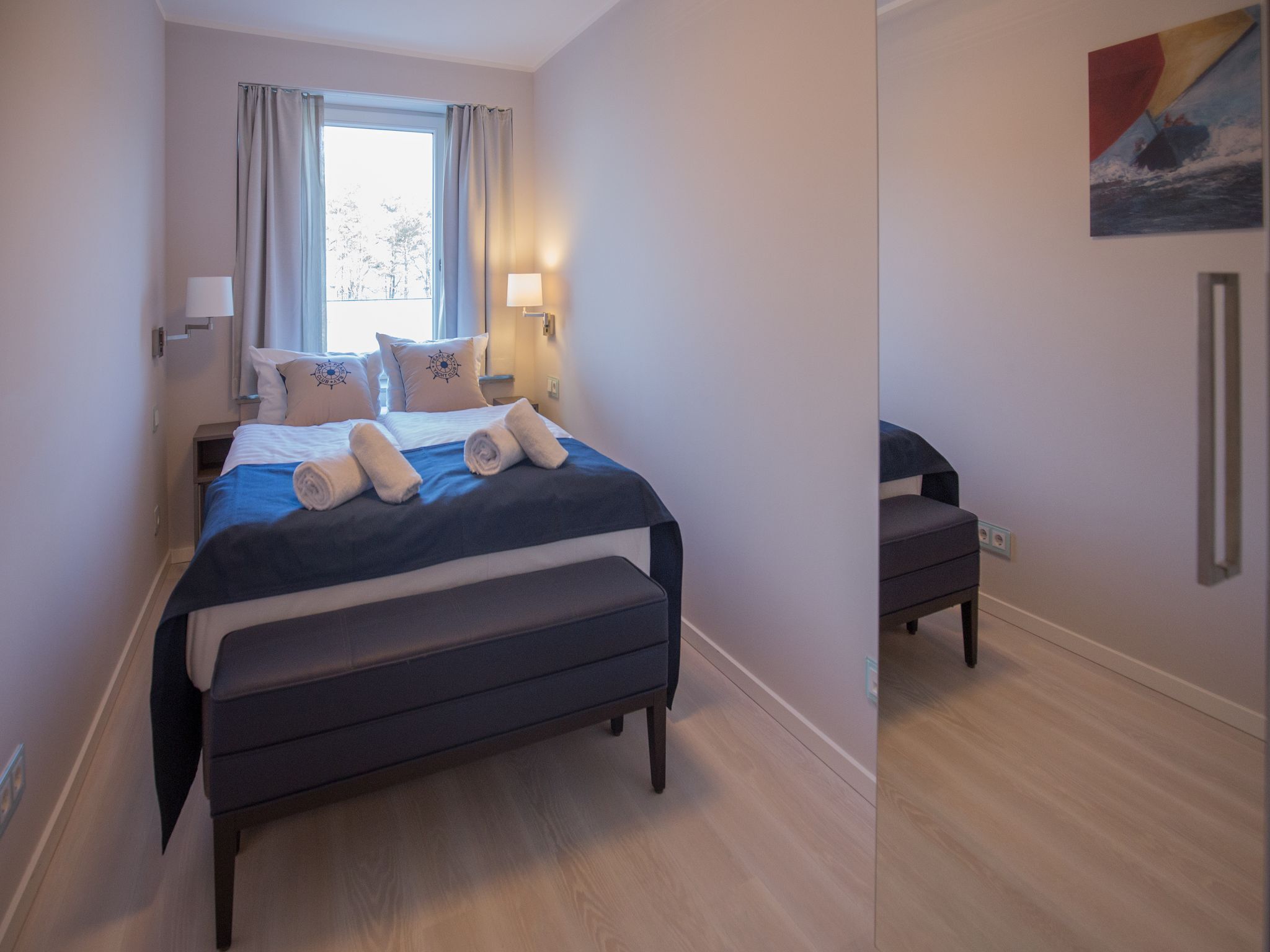 A modern hotel room with a large bed, bedside lamps, a bench, and a painting on the wall.