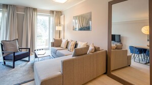 A modern living room with a sofa, armchair, and a dining area with chairs. - Beautiful apartment in top beach location with sea view (Ostseebad Binz)