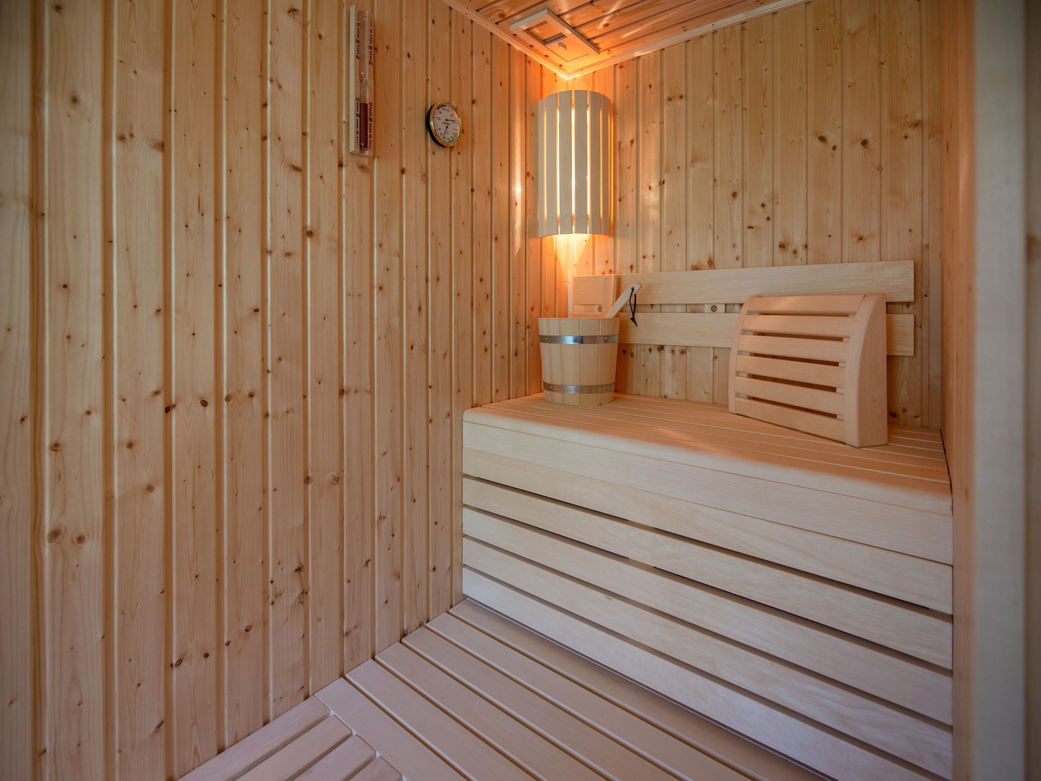 Een houten sauna met een bank, een klok aan de muur en een cilindrische kachel.