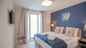 Hotellihuone, jossa on suuri sänky, seinälle asennettu televisio, taulu ja ikkunasta avautuva näkymä ulos.