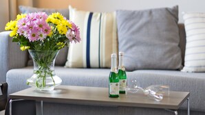 Un vase en verre transparent contenant des fleurs jaunes et roses, posé sur une table, ainsi que deux bouteilles vertes et un verre à vin.