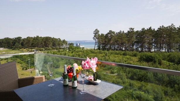 Un balcon avec une table dressée pour un repas, offrant une vue sur un paysage côtier avec des arbres et la mer.