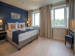 A hotel room with a large bed, two bedside tables, a desk, and a window with curtains. - Apartment with sea view, 2 bedrooms and balcony (Ostseebad Binz)