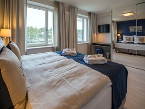 A hotel room with a large bed, a desk, a chair, and a TV. - Apartment with a view of the ocean, 2 bedrooms, and a balcony (Ostseebad Binz)