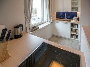 A modern kitchen with a built-in stove, a coffee maker, and a window with curtains. - Apartment with sea view, 2 bedrooms and balcony (Ostseebad Binz)