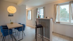 Uma sala de jantar moderna com mesa e cadeiras, uma luminária pendente, um radiador e uma janela com cortinas.