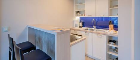 A compact kitchen with white cabinets, a sink, and a coffee machine. There are two chairs and a small table.