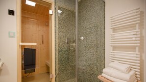 Un cuarto de sauna con puerta de madera, zona de ducha con vidrio y un perchero con toallas dobladas.