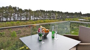 Un balcón con una mesa lista para una comida, con vistas a un área boscosa y una masa de agua.