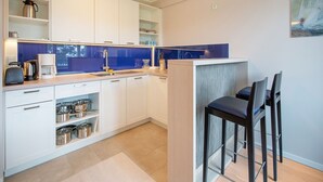 Una cocina moderna con armarios blancos, un salpicadero azul y una pequeña zona de comedor con dos sillas.