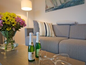 A living room with a sofa, a vase of flowers, two bottles of wine, and a wine glass on a wooden table. - Apartment with sea view, 1 bedroom and balcony (Ostseebad Binz)