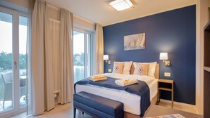 A hotel room with a large bed, a bench, a nightstand, and a view of the outdoors. - Apartment with sea view, 2 bedrooms and balcony (Ostseebad Binz)