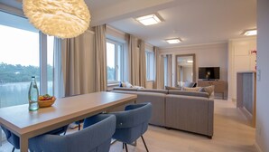 A modern living room with a sofa, a dining table with chairs, and a television. - Apartment with sea view, 2 bedrooms and balcony (Ostseebad Binz)