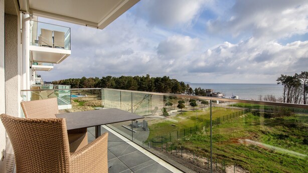 A balcony with wicker furniture, a glass railing, and a view of the sea and greenery. - Apartment with sea view, 2 bedrooms and balcony (Ostseebad Binz)