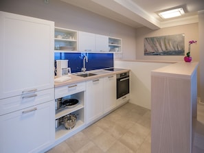 Une cuisine moderne avec des meubles blancs, un pare-feu bleu et un tableau représentant des voiliers accroché au mur.