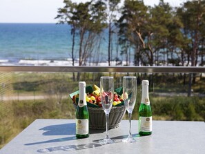 A table with two bottles of Schlosser Kylling wine, a fruit basket, and three wine glasses on a balcony overlooking the ocean. - Apartment with sea view, 2 bedrooms and balcony (Ostseebad Binz)