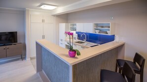A modern kitchen with white cabinets, a blue backsplash, and a central island with a pink vase. There are two dark chairs and a TV in the room. - Apartment with sea view, 2 bedrooms and balcony (Ostseebad Binz)