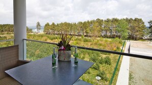 Een balkon met een tafel voor twee, met uitzicht op een kustlandschap met bomen en een strand.