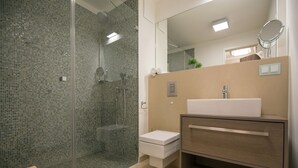 Een moderne badkamer met een glazen douchecabine, een wit wastafeltje en een houten badkamerkast.