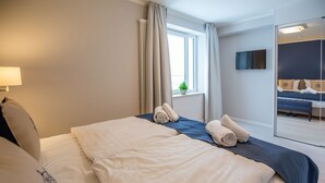 Quarto de hotel com uma cama grande, uma televisão fixada na parede e vista para outro quarto.