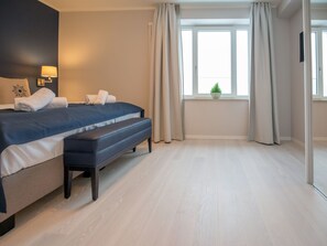 A modern hotel room with a large bed, a bench, a nightstand with a lamp, a window with curtains, and a small plant on the windowsill. - Apartment with sea view, 1 bedroom and balcony (Ostseebad Binz)