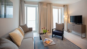 Quarto de hotel moderno com sofá, poltrona, TV e uma mesa com flores.