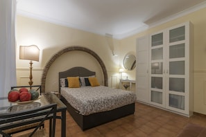 Une chambre à coucher avec un lit, un bureau avec une lampe, une chaise, un miroir rond et une armoire.