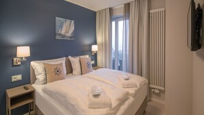 A hotel room with a large bed, two bedside tables, a nightstand, a painting on the wall, a window with curtains, and a radiator. - Sky suite with unobstructed sea view, roof terrace and balcony (Ostseebad Binz)